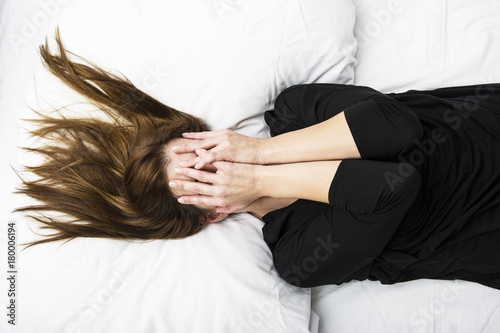 Young depressed woman is lying in her bed, covering her face with her hands. Sorrow concept.  photo