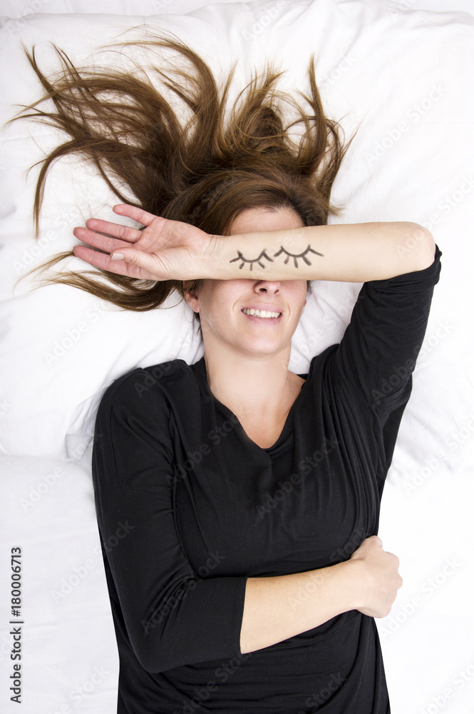 young woman is lying in her bed, joking. She is replacing her eyes by covering it with her painted arms. Lifestyle concept. young woman is lying in her bed, joking. She is replacing her eyes by covering it with her painted arms. Lifestyle concept.