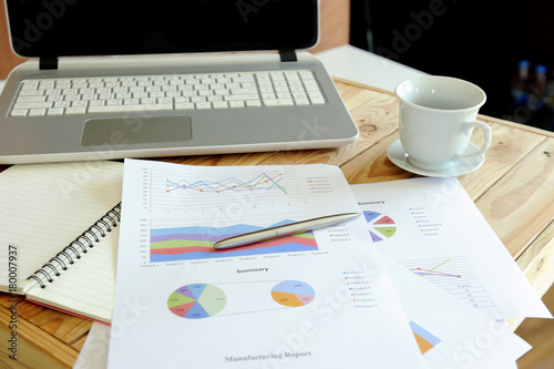 Messy working table with laptop, blank notebook, diagram business chart and cup of coffee