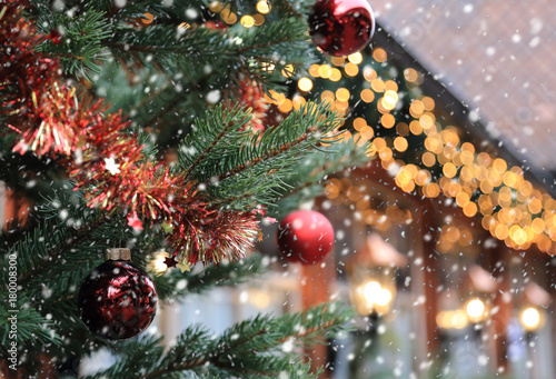 Christmas street decorations and falling snow - red ball, fir and bokeh lights