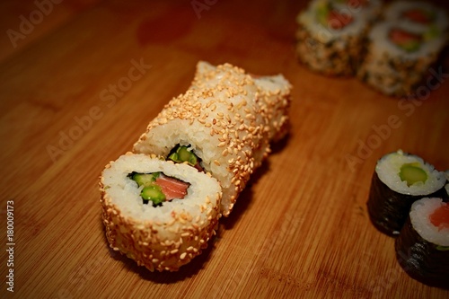Sliced Japanese sushi roll maki with rice, salmon, avocado and cucumber covered with sesame seeds on wooden table