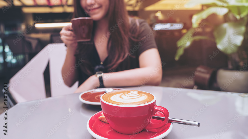 Closeup image of a beautiful Asian woman holding and drinking coffee with latte coffee cup on glass table in loft cafe