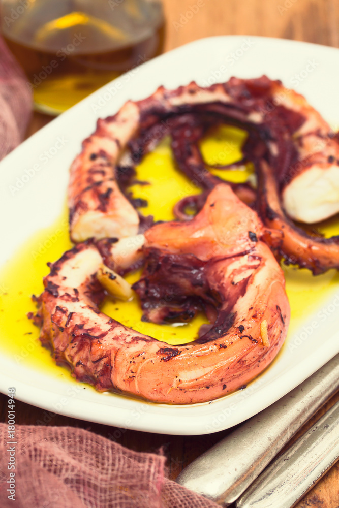 grilled octopus with garlic on white dish on wooden background