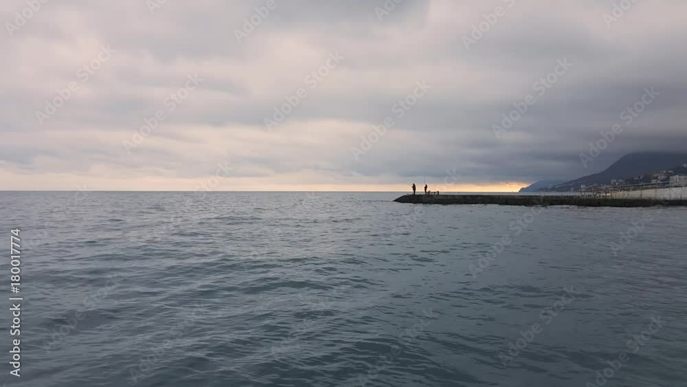 Fishermen are fishing from abandoned pier / Fishermen standing on abandoned pier near seashore in early evening