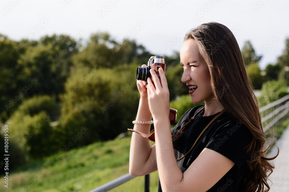 Young happy female photographer walks in the Park with retro camera