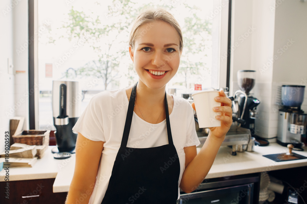 Portrait of happy beautiful young Caucasian smiling woman barista drinking from paper cup. Person resting relaxing at work place Portrait of happy beautiful young Caucasian smiling woman barista drinking from paper cup. Person resting relaxing at work place