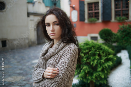 Young woman wearing woolen gray sweater walking in the spring city street. Warm soft cozy image. Cold weather. Copy space