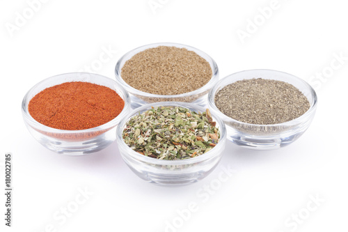 Ground black pepper, paprika, coriander and italian herbs in glass bowls isolated on white background