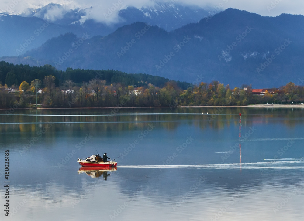 Serenity morning on Alpine lake with red boat and foggy mountains