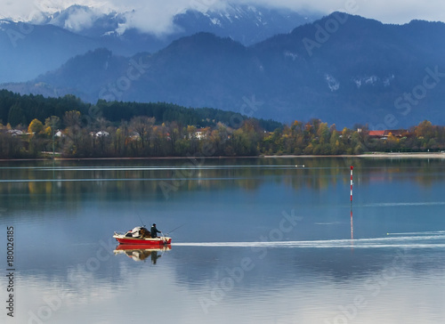 Serenity morning on Alpine lake with red boat and foggy mountains