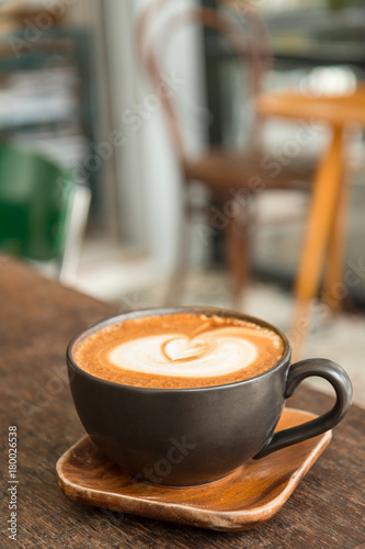 Hot latte coffee with latte art in a matt black cup on the wooden table in a coffee shop background
