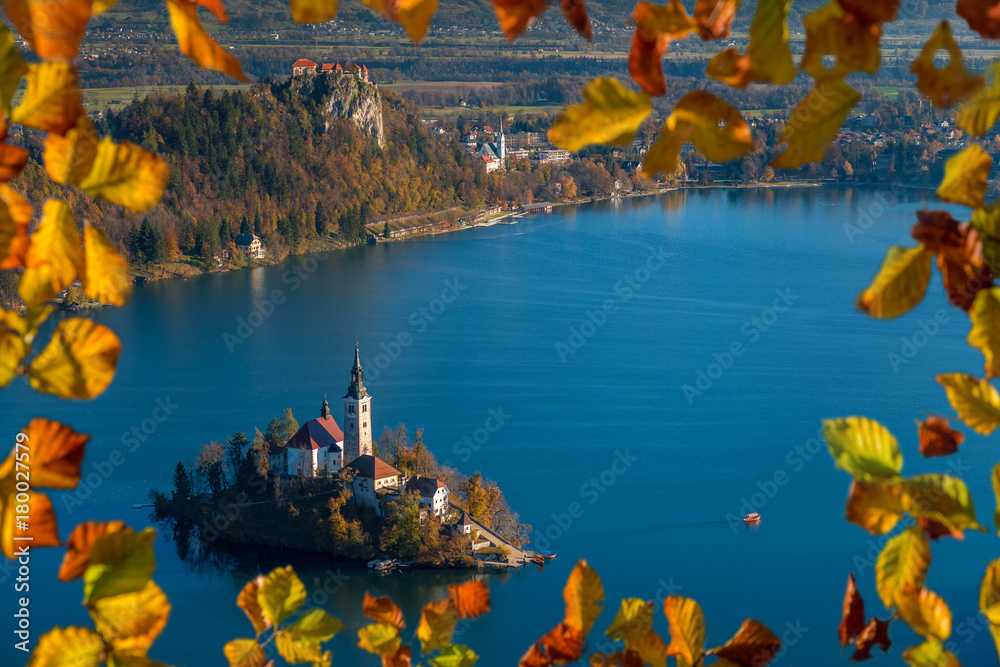 Bled, Slovenia - Sunrise at lake Bled taken from Osojnica viewpoint with traditional Pletna boat and Bled Castle at background at autumn. Framed with autumn foliage