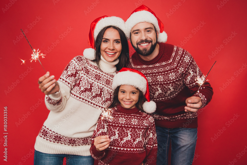 Fototapeta premium Cheerful relatives celebrate with sparkles, married couple, small cute adorable girl, in knitted traditional x mas costumes, head wear, beaming smiles, happiness