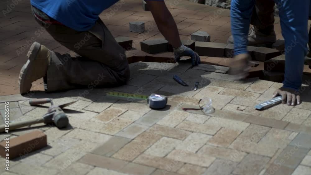 Closeup shot of two men fitting custom cut bricks into a brick paver design as part of a hardscaping project. Closeup shot of two men fitting custom cut bricks into a brick paver design as part of a hardscaping project.