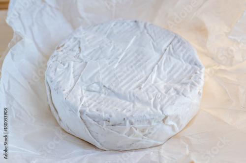 Camembert or brie cheese in white paper on wooden background