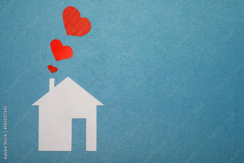 Concept of love in house. White paper house on blue textured background with red hearts from pipe. Smoke from pipe in form of paper red hearts. LOVE, family, home.