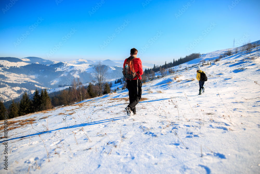 Young couple hiking outdoors with backpacks in winter mountains. Rear view shot of young woman with her boyfriend in the mountains. Hikers with backpacks. Travel concept