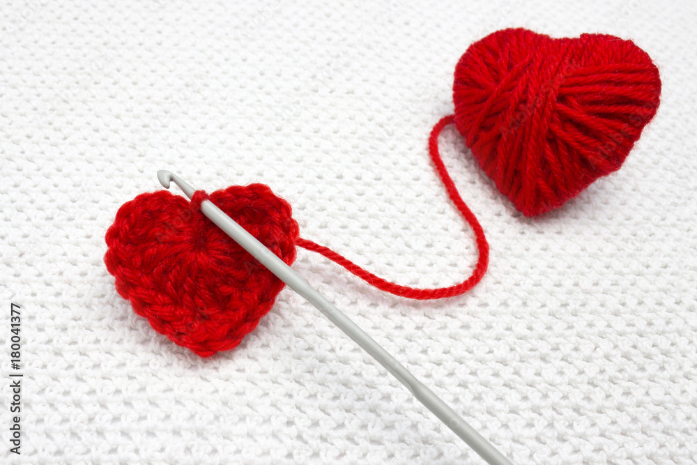Old metal crocheting hook and red yarn ball like a heart on the white  crochet background.