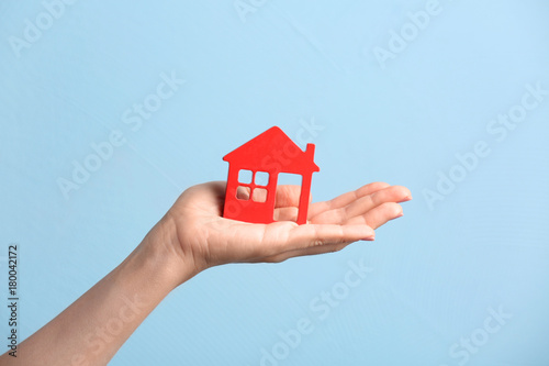 Woman holding wooden figure of house on color background