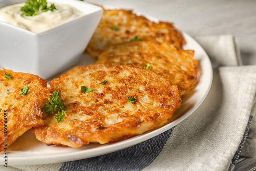 Plate with Hanukkah potato pancakes and sauce on table, closeup