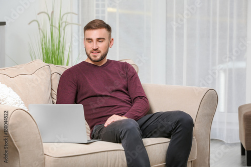 Young man with modern laptop on sofa at home
