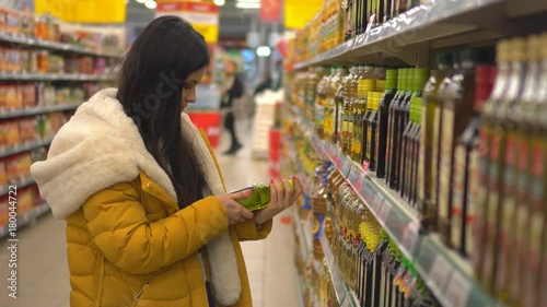 Woman chooses oil in the supermarket. Shopping in the store. Young female carefully analyzing products in a market.