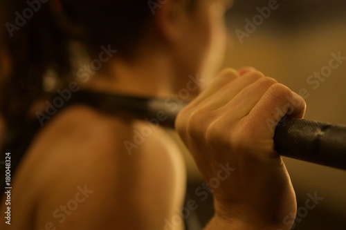 Close-up on the hand of a female weight lifter with a barbell on her back