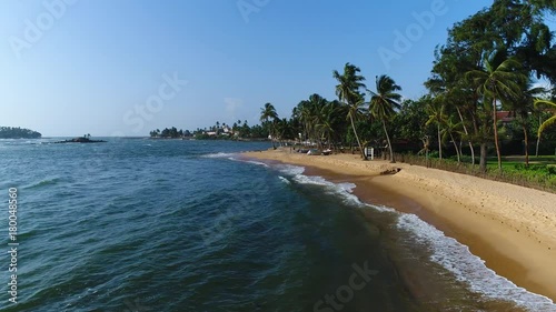 Aerial of sandy beach with palm trees, which is washed by sea on a sunny day in Sri Lanka