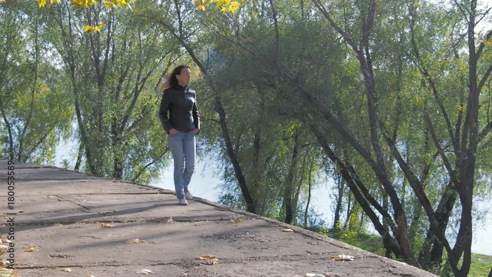 A woman is walking along the autumn embankment of the river. A woman is walking along the autumn embankment of the river.