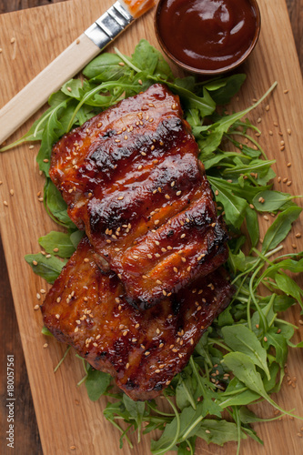 Closeup of pork ribs grilled with BBQ sauce and caramelized in honey on a bed of arugula. Tasty snack to beer on a wooden Board for submission on the old wooden background. Top view photo