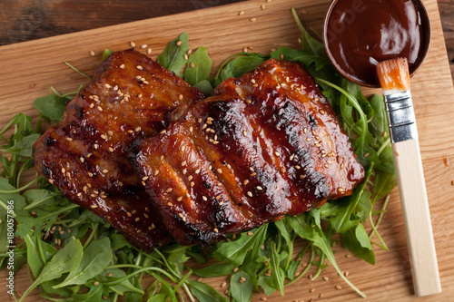 Closeup of pork ribs grilled with BBQ sauce and caramelized in honey on a bed of arugula. Tasty snack to beer on a wooden Board for submission on the old wooden background. Top view photo