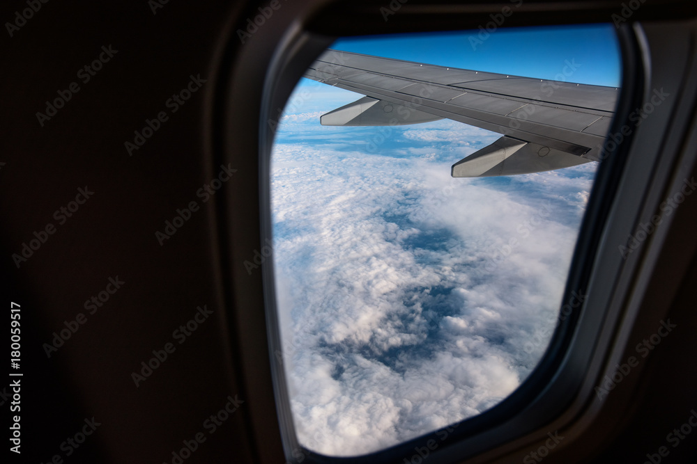 Airplane window from inside. Through the window you can see clouds and airplane wing.