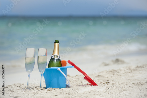 champagne and glasses in sand bucket on tropical beach