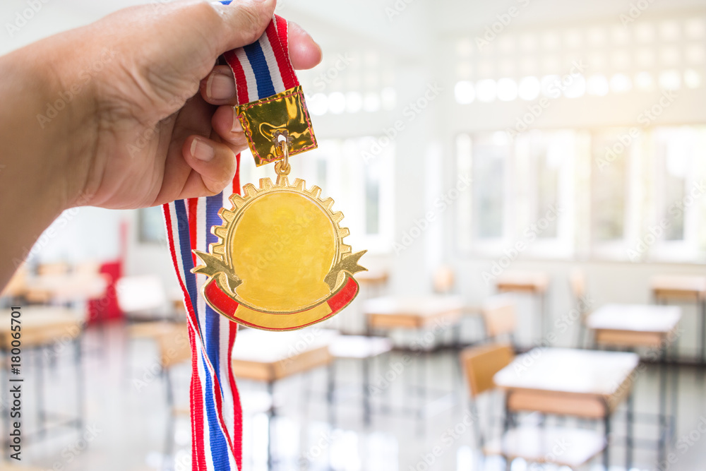 Students hands raised holding two gold medals with Thai ribbon against blur empty classroom at school background, Show success in studying, Winners success awards in educational concept.