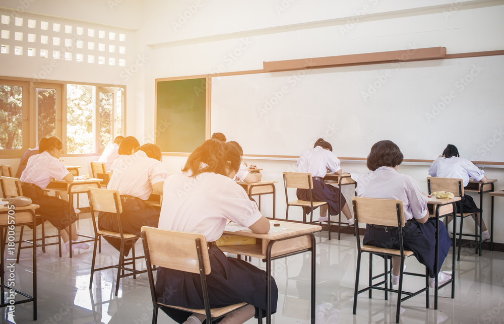 Behind girls group undergraduate students testing of examination in room and student sitting on row chair doing final exams in classroom with Thailand uniform. Asian Education Concept. Behind girls group undergraduate students testing of examination in room and student sitting on row chair doing final exams in classroom with Thailand uniform. Asian Education Concept.