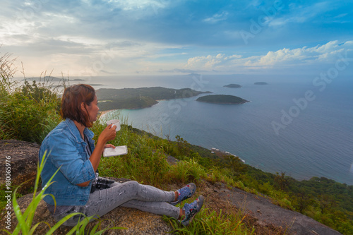 a lady drinking coffee on the highest viewpoint name Pha Hin Dum. on Pha Hin Dum viewpoint can see around Phuket island. Niharn beach wind turbine Phomphep cape Rawai beach are in front of Pha Hin Dum