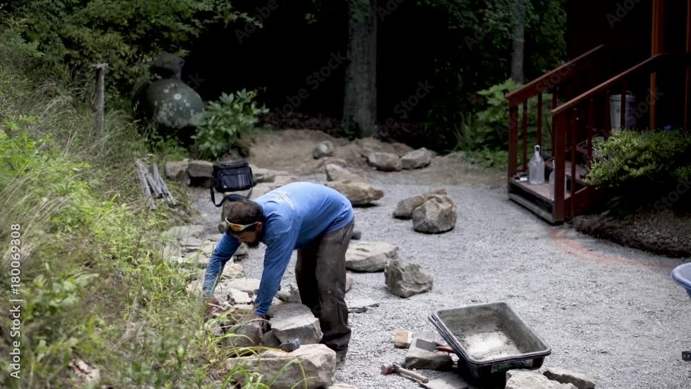 Looking down onto a hardscaper putting putting a rock into a stone wall under construction. Looking down onto a hardscaper putting putting a rock into a stone wall under construction.