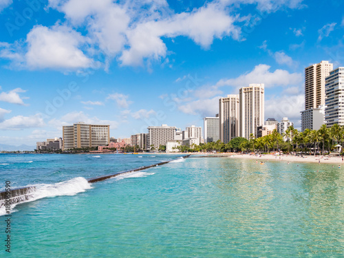 Blue Waters of Queens Beach and pier in Waikiki with Hotels in the distance, Honolulu, Oahu Island, Hawaii, USA. Waikiki Beach in the center of Honolulu has the largest number of visitors in Hawaii.