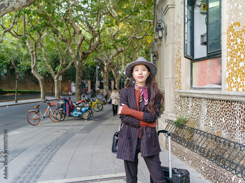 Beautiful Chinese woman in suit stand at the corner of street with suitcase beside her.