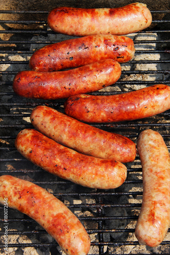 Bratwursts on a grill. Close up composition of grilled outdoor brat sausages during good weather 4th of July picnic. Lifestyle background, unhealthy eating concept.. Vertical composition.