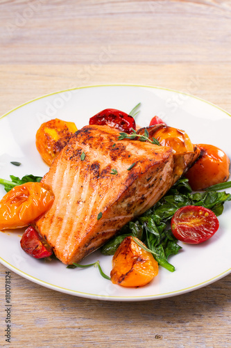 Salmon fillet with spinach and tomatoes on white plate on rustic wooden background