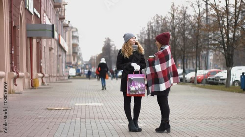 Two girls after the festive shopping consider the gifts. Slow motion. Two young pretty girls stand on the street and holding bags with shopping.