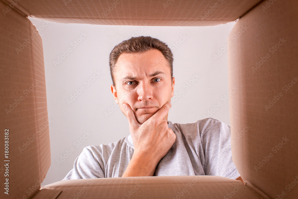 Naklejka premium Man surprised, unpacking and opening a carton gift box, and looking inside. View from the box