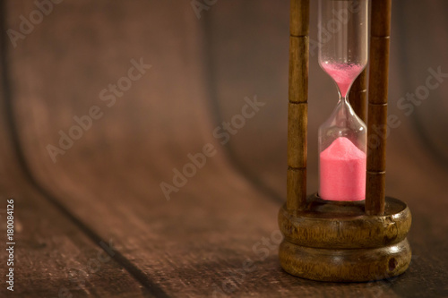 Hour Glass with pink sand on wooden background