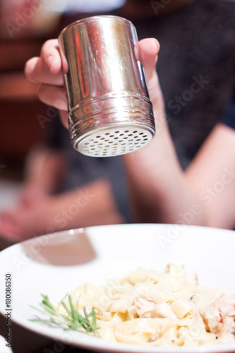 Female hand throws salt from cellar into white plate of homemade pasta pici with Bolognese sauce . photo