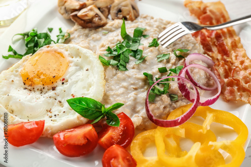 Oatmeal porridge, fried egg and garnish on plate, closeup