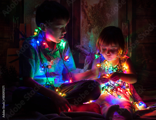 Boy and girl sitting on the floor and playing with Christmas light