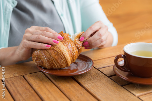 Fényképezés Woman with pink manicure is tearing a small piece from large croissant , aliened