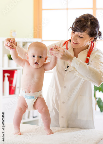 Pediatrician examining cute baby boy and testing his walking reflex photo