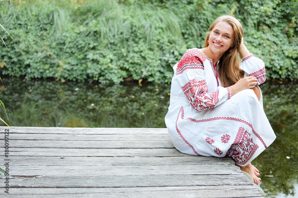 Naklejka premium Beautiful slavonic girl with long blond hair and blue eyes sitting near river